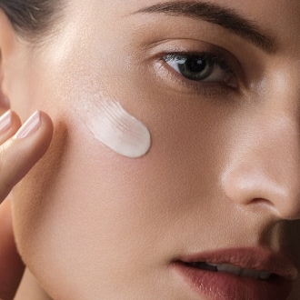 Close up of model applying Crème de la Mer to cheek, in bright, ambient lighting