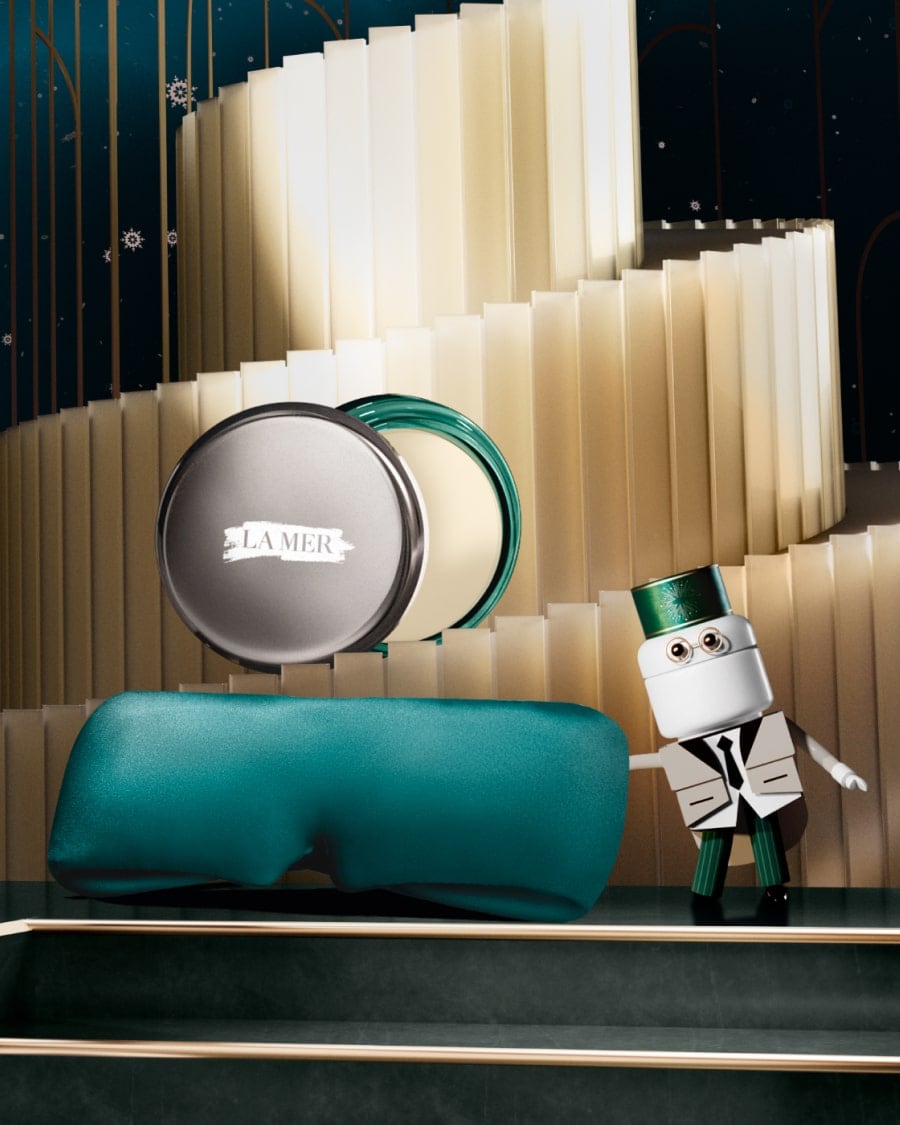 3 separate La Mer lip products nestled in snow, next to La Mer attendant caricature, with animated snow falling from the sky