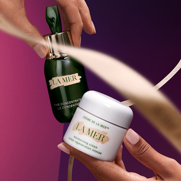 hands holding la mer products on pink background